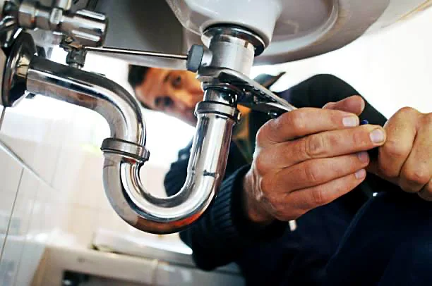 Plomero profesional reparando el sifón de un lavabo con llave perica